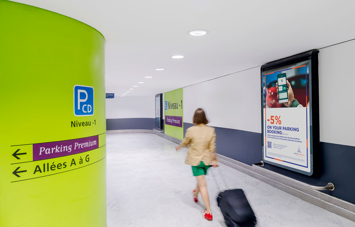 A woman with her cabin suitcase walks through the corridor of an official Paris Airport parking lot
