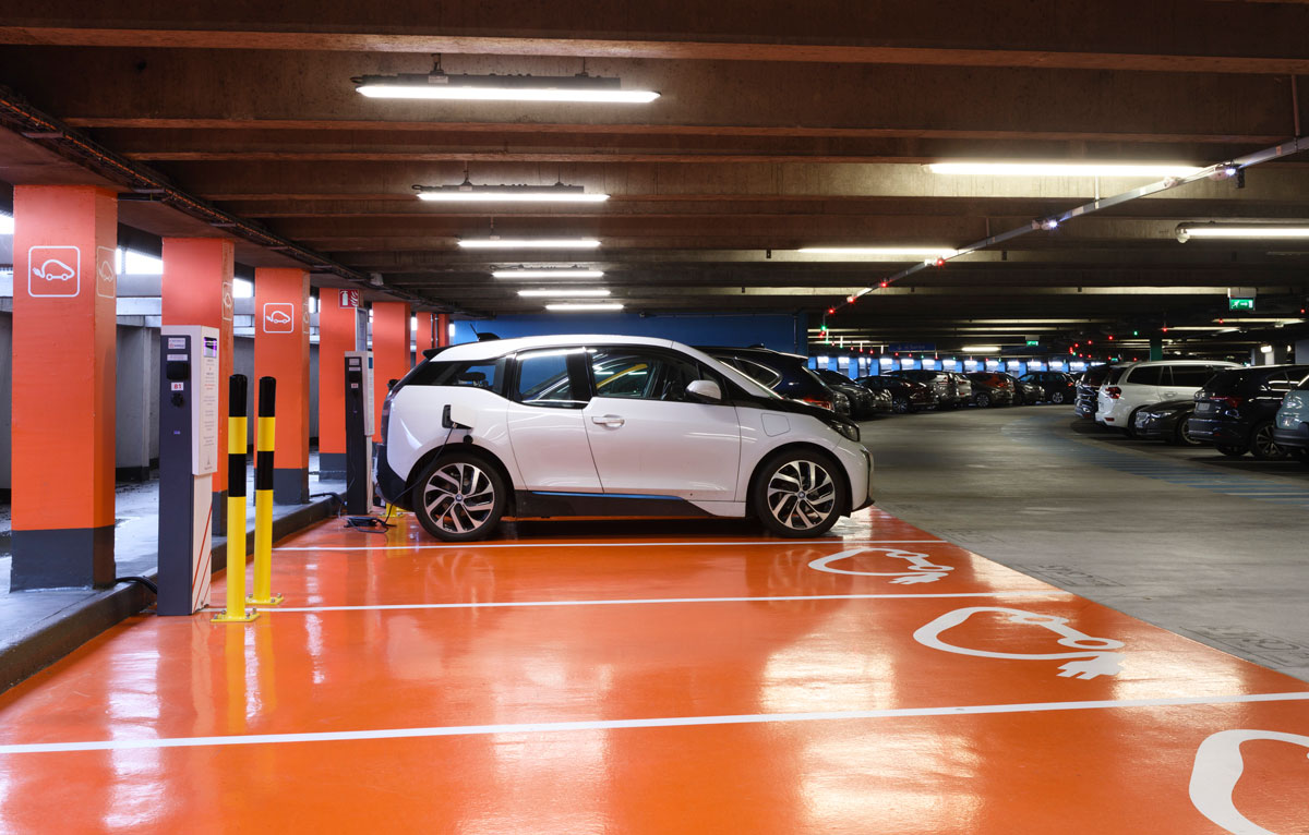 A white car parked in the electric vehicle zone of a Paris Airport parking lot